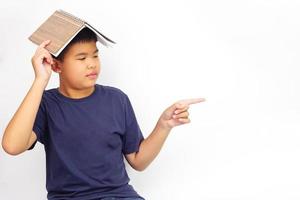 A picture of a boy in glasses point to the side and covering his head with a book. Education and learning concept. photo