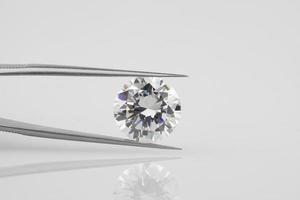 Round Diamond Held in Tweezers. Horizontal Gemstone Photograph on Grey Background with Reflection. photo