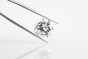 diamante sostenido dentro de pinzas. gran diamante redondo, angulado y reflejado en un fondo pálido. foto