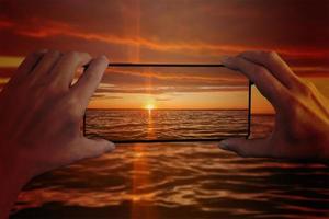 la niña fotografía la puesta de sol en el mar en un teléfono inteligente. primer plano de las manos y el teléfono inteligente. foto