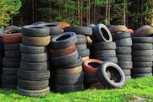 A pile of old car tires lies on the grass against the background of the forest. Ecology concept. photo