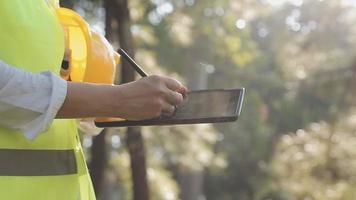 intelligenter asiatischer arbeiter oder männlicher bauingenieur mit schutzhelm und reflektierender weste mit digitalem tablet zur projektplanung und prüfung der bauzeichnung auf der baustelle. video