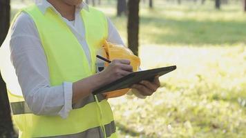 slim Aziatisch arbeider Mens of mannetje civiel ingenieur met beschermend veiligheid helm en reflecterende hesje gebruik makend van digitaal tablet voor project planning en controle bouwkundig tekening Bij bouw plaats. video