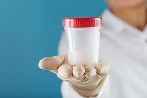 A doctor's gloved hand holding a bottle of a container with a sperm sample for medical analysis. photo