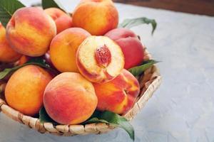 Ripe peaches in a wicker basket on a stone gray table with a juicy peach slice with a stone pit. photo