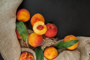 Peaches on a black background with burlap fabric and green leaves. Sweet and juicy peach slices with a stone photo