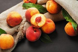 Peach fruit on a black background with a cloth of burlap and green leaves. photo