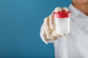 A doctor's gloved hand holding a bottle of a container with a sperm sample for medical analysis. photo