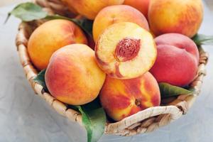 Ripe peaches in a wicker basket on a stone gray table with a juicy peach slice with a stone pit. photo