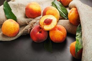 Peaches on a black background with burlap fabric and green leaves. Sweet and juicy peach slices with a stone photo