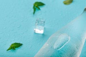 Bottle with an ice cold beverage, ice cubes, drops and mint leaves on a blue background. photo