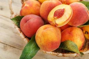 Peaches in a basket on a wooden background with a slice of sliced juicy peach with a stone. photo