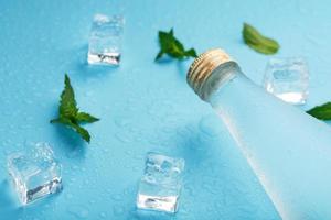 Cold Water Bottle, ice cubes, drops and mint leaves on a blue background. photo