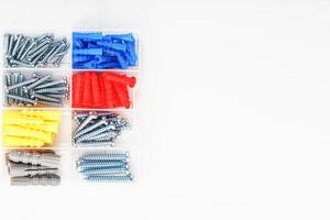 Screws and dowels of various sizes, types and colors in a transparent plastic box. photo