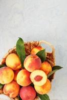 Ripe peaches in a wicker basket on a stone gray table with a juicy peach slice with a stone pit. photo