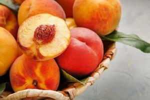 Ripe peaches in a wicker basket on a stone gray table with a juicy peach slice with a stone pit. photo