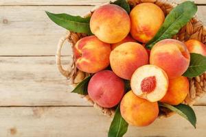 Peaches in a basket on a wooden background with a slice of sliced juicy peach with a stone. photo