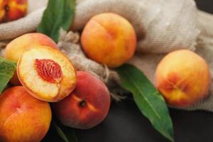 Peach fruit on a black background with a cloth of burlap and green leaves. photo