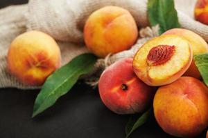 Peaches on a black background with burlap fabric and green leaves. Sweet and juicy peach slices with a stone photo