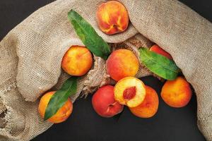 Peach fruit on a black background with a cloth of burlap and green leaves. photo