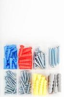 Box with screws and dowels of different sizes, shapes and colors on a white background. photo