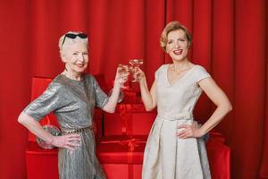 dos mujeres maduras y mayores celebrando el año nuevo sosteniendo en las manos copas de vino espumoso blanco. navidad, familia, amigos, celebración, concepto de año nuevo foto