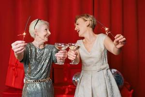 Two beautiful stylish mature senior women in dresses with sparklers and glasses celebrating new year. Christmas, family, friends, new year, Fun, party, style, celebration concept photo