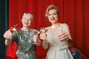 Two beautiful stylish mature senior women in dresses with sparklers and glasses celebrating new year. Christmas, family, friends, new year, Fun, party, style, celebration concept photo