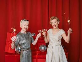 Two beautiful stylish mature senior women in dresses with sparklers and glasses celebrating new year. Christmas, family, friends, new year, Fun, party, style, celebration concept photo