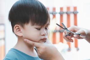 Asian mother cuts her son's hair by herself at home. Happy haircut ideas for kids. Mothers are happy to cut their children's hair. photo