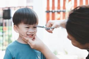 Asian mother cuts her son's hair by herself at home. Happy haircut ideas for kids. Mothers are happy to cut their children's hair. photo