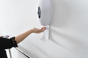 woman's hand using alcohol gel with automatic machine in the hospital for cleaning hands. Economical and clean infection prevention concept in the state medical center area. disinfection photo