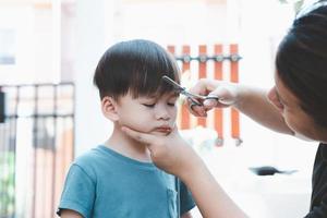 Asian mother cuts her son's hair by herself at home. Happy haircut ideas for kids. Mothers are happy to cut their children's hair. photo