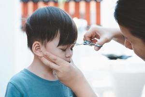 Asian mother cuts her son's hair by herself at home. Happy haircut ideas for kids. Mothers are happy to cut their children's hair. photo