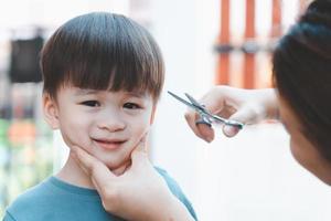 Asian mother cuts her son's hair by herself at home. Happy haircut ideas for kids. Mothers are happy to cut their children's hair. photo