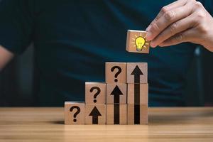 Hand of business selected wooden cube block with light bulb icon symbol and icon question mark creative concept. new ideas photo