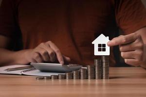 Businessman holding house icon with calculator and pile of money. concept saving money to buy real estate, buy a house, collecting money, financial planning, save money for the future photo