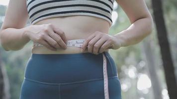 hermosa mujer gorda con cinta métrica usa su mano para exprimir el exceso de grasa que está aislado en un fondo blanco. ella quiere perder peso, el concepto de cirugía y descomponer grasa bajo el video