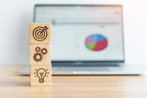 dartboard above Gear and Lightbulb icon block against laptop with business data graph on table. business planning process, goal, strategy, target, mission, action, objective, teamwork and idea concept photo