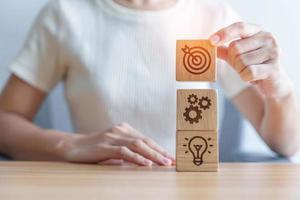 Woman hand holding dartboard above Gear and Lightbulb icon block. business planning process, goal, strategy, target, mission, action, objective, teamwork and idea concept photo