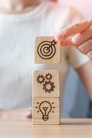 Woman hand holding dartboard above Gear and Lightbulb icon block. business planning process, goal, strategy, target, mission, action, objective, teamwork and idea concept photo