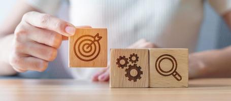 Woman hand holding dartboard, Gear and Lightbulb icon block on table. business planning process, goal, strategy, target, mission, action, objective, teamwork and research concept photo
