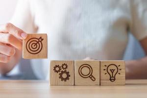 Woman hand holding dartboard above Gear, magnifying and Lightbulb icon block. business planning process, goal, strategy, target, mission, action, research, teamwork and idea concept photo