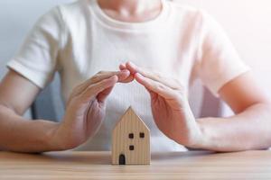 Businesswoman hand cover wooden Home model. real estate, house insurance, inflation, recession economy and property concepts photo