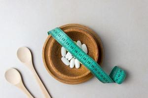 A handful of pills in a wooden plate covered with measuring tape. Surrounded by wooden spoons. The concept of weight loss, diet, medicine for weight loss. Top view photo