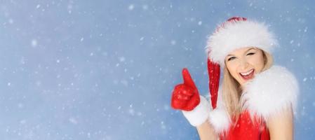 Woman in a Santa Claus hat smiles, winks and shows a like thumb with a red mitten photo