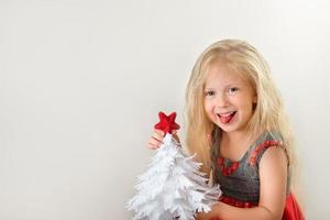 niña sonriente con árbol de navidad de papel blanco y estrella roja en sus manos foto