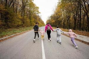 Back of mother with four kids running on road at autumn fall forest. photo