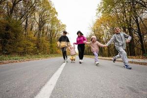madre con cuatro hijos corriendo en la carretera en el bosque de otoño. foto