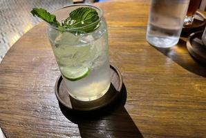 Selective focus, Delicious refreshing summer mojito with ice, lime and mint in a glass with grops. wood background photo